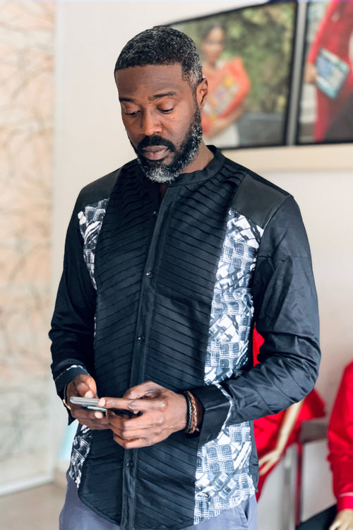 Man wearing a black and white patterned shirt using a phone indoors.