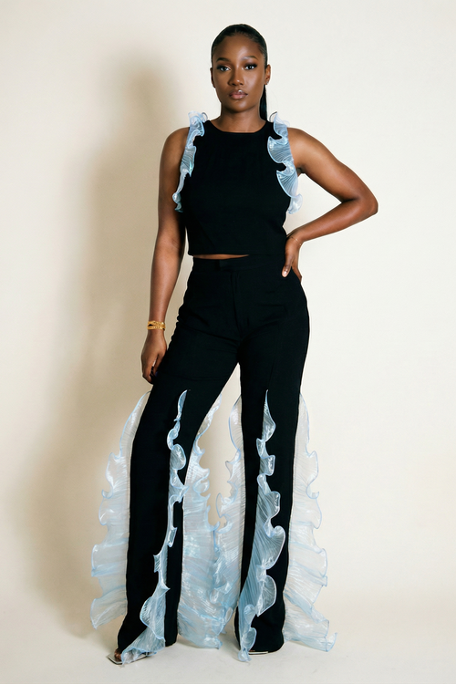 Woman wearing a black outfit with ruffled sleeves and pants on a beige background